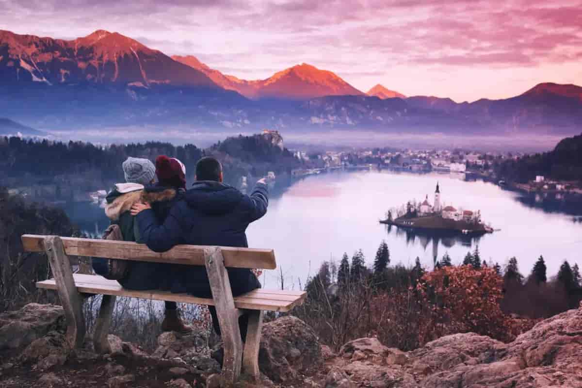 Couple on bench viewing Lake Bled island church and mountains at sunset