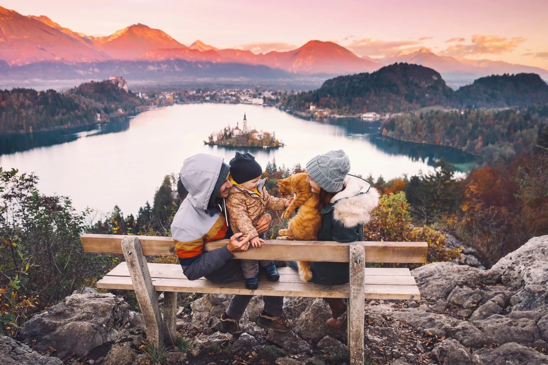 Family with cat on bench overlooking Lake Bled island and Julian Alps at sunset