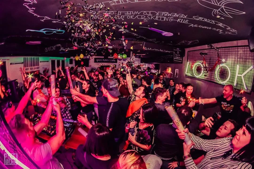 Crowd celebrating indoors with confetti falling from the dark ceiling decorated with white drawings.