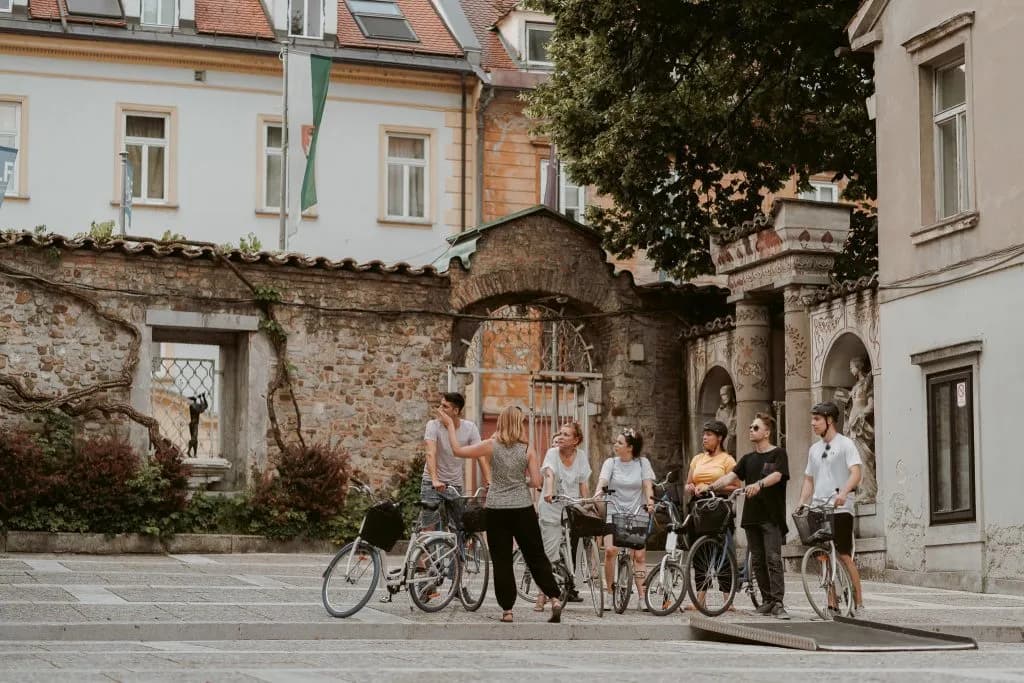 Guided bike tour group listening to instructor near historic stone wall in Ljubljana