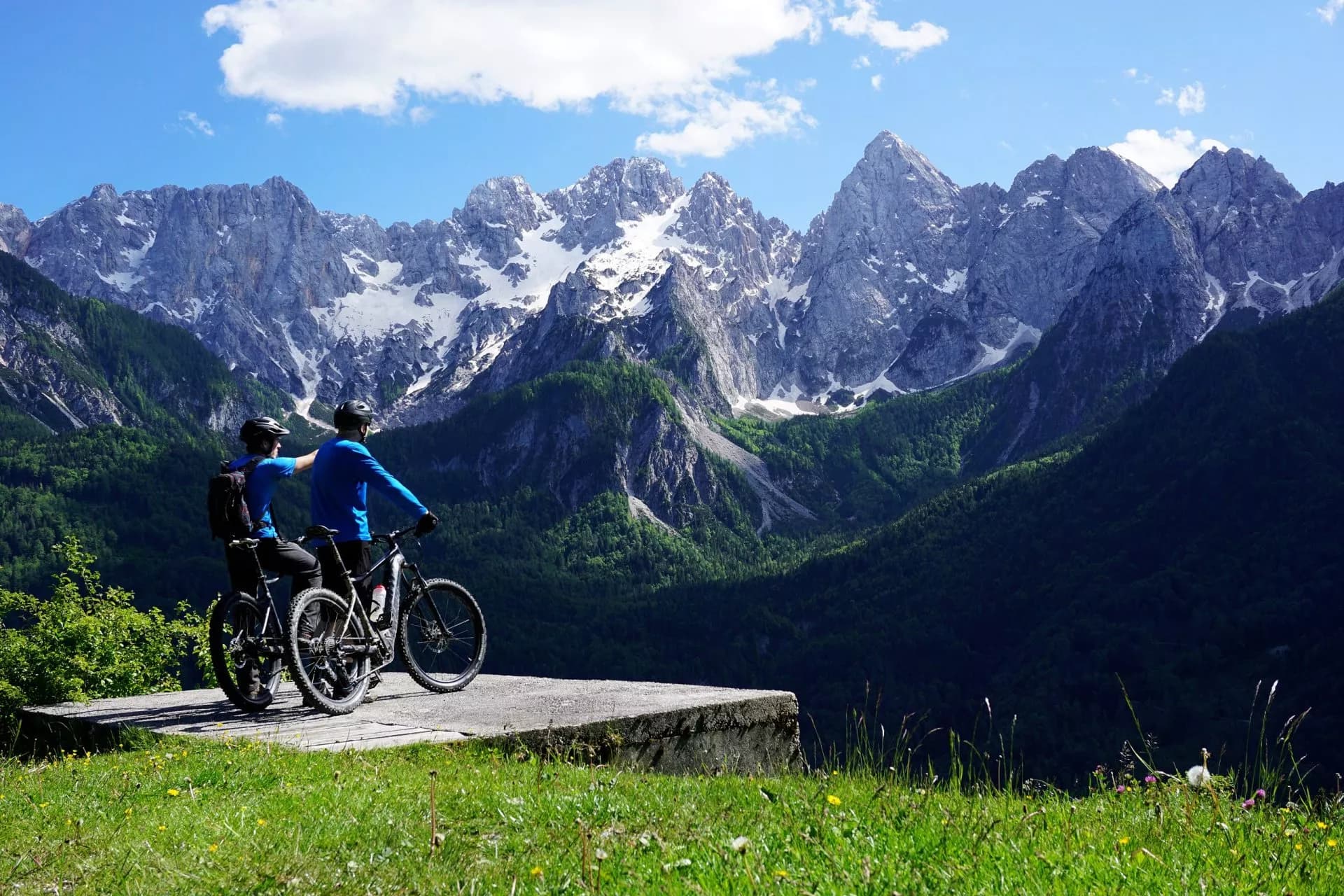 Mountain bikers viewing snow-capped Julian Alps in spring from a grassy overlook