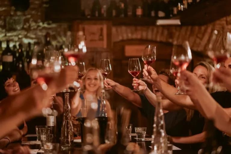 People toasting with glasses of red wine during a tasting in a dimly lit cellar setting.