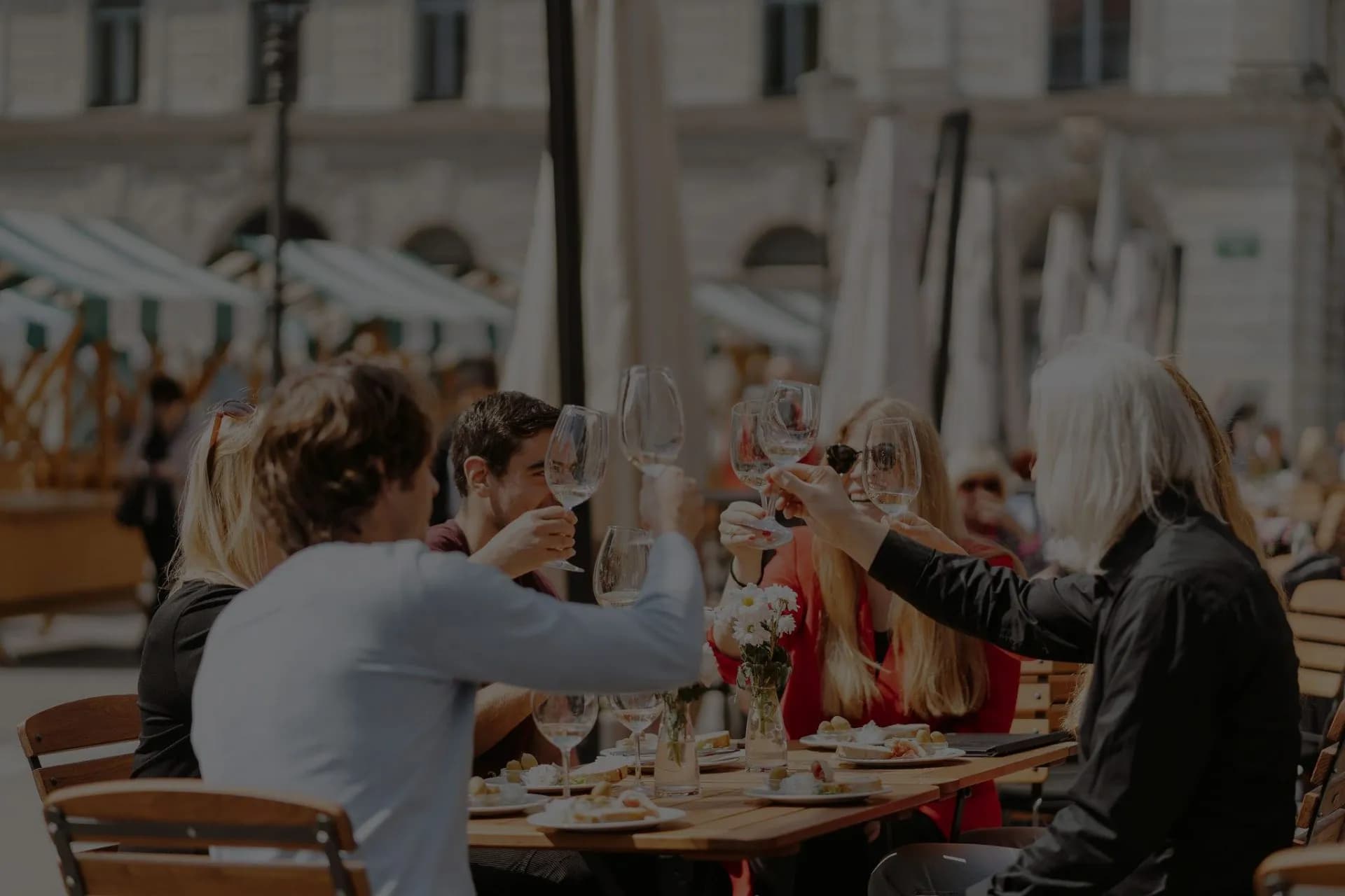 Friends toasting with wine glasses at an outdoor cafe table in Ljubljana.