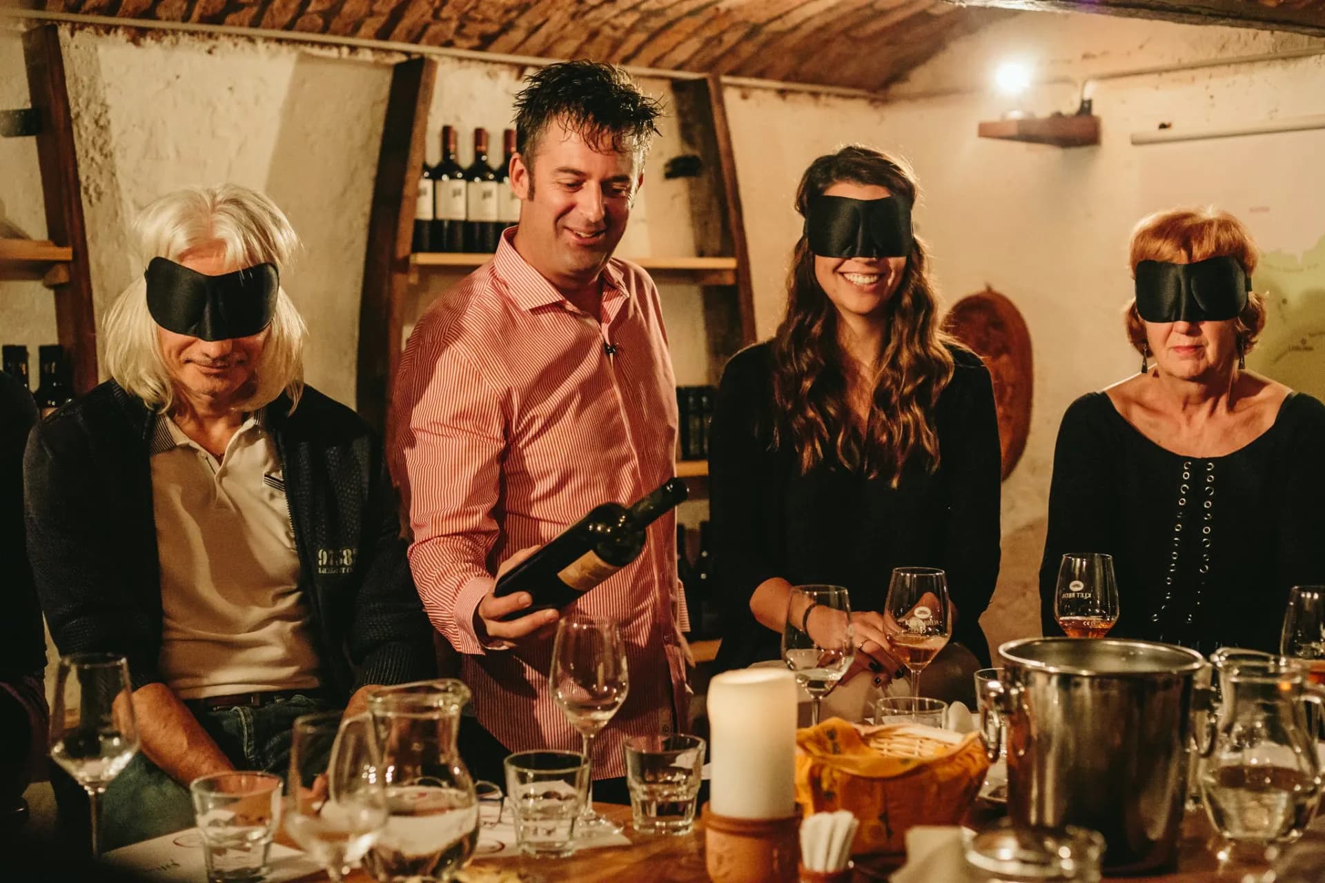 Wine tasting in cellar with participants blindfolded, man holding a bottle